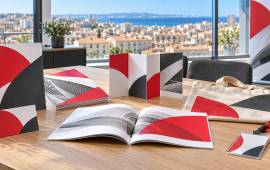 Brochures, cartes, dépliant, badge, roll-up et sac personnalisé dans un bureau lumineux avec vue sur les toits de Marseille.