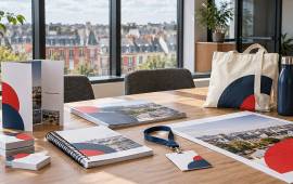 Cartes, brochures, dossier relié, badge, sac et gourde personnalisés dans un bureau avec vue sur les toits d’ardoise de Rennes.